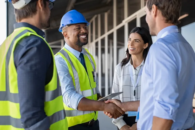 Smiling contractor in a hard hat shaking hands with homeowners